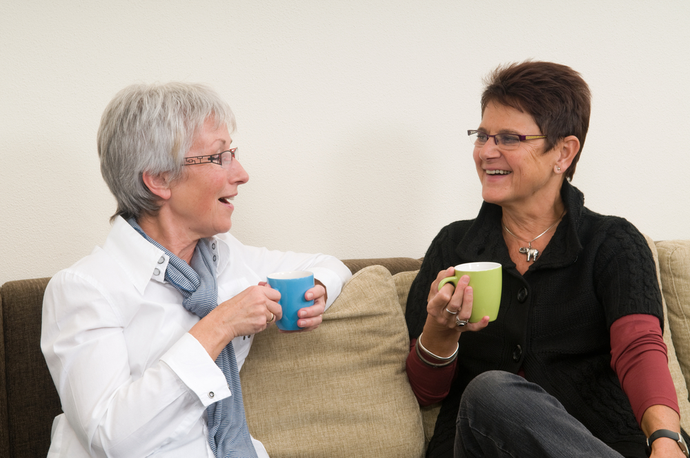 two mature women having coffee seated on a couch