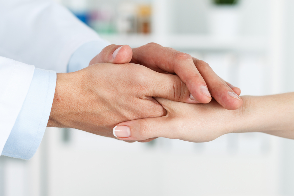 Friendly male doctor's hands holding female patient's hand for encouragement and empathy