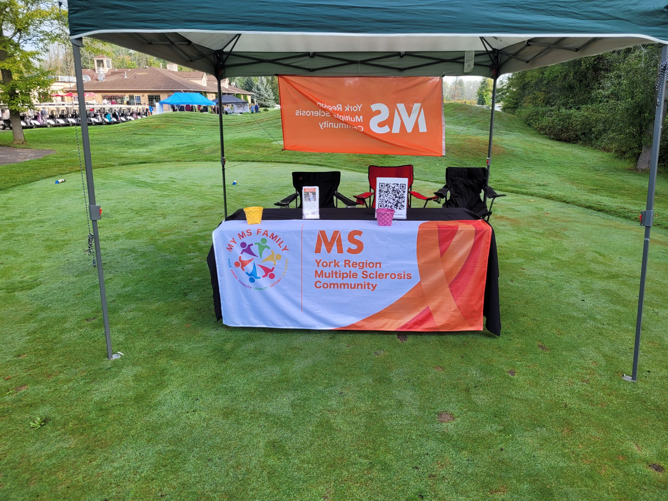 A booth under a canopy on a grassy field with a banner reading "MS York Region Multiple Sclerosis Community